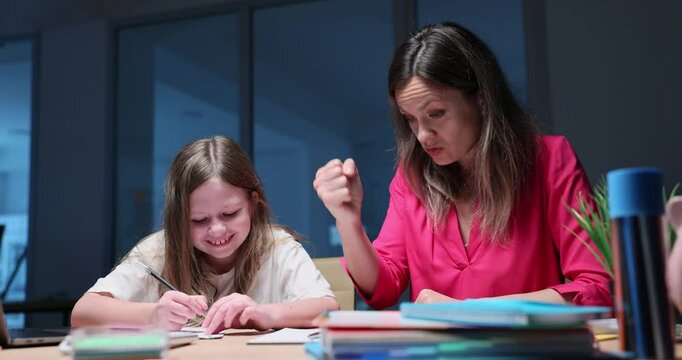 Worried mother taps fist on table scolding smiling daughter at desk. Irritated woman controls naughty schoolgirl learning lesson at home slow motion