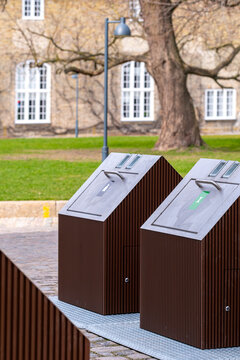 Integrated public trash and recycling units in Copenhagen park area, designed with brown panels and icons, blending function and clean Scandinavian design.