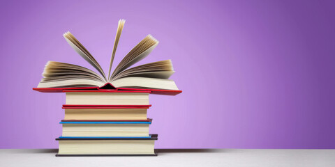 Fototapeta premium Stack of colorful books with open pages against purple background, space for text, banner