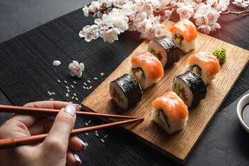 Set of sushi, maki rolls, hand with chopsticks and branch of white flowers on stone table