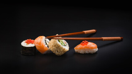 Sushi with red caviar and chopsticks on a black table. Macro