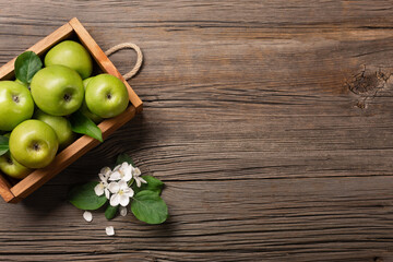 Ripe green apples with branch of white flowers in wooden box on a wooden table