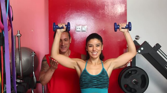 Woman lifting weights with personal trainer in gym