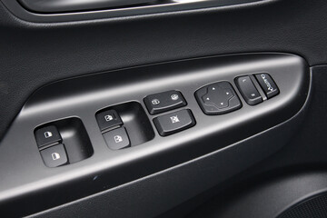 Obraz premium Window control buttons in modern electric car. Car leather interior details of door handle with windows controls and adjustments. Door trim. Modern car interior details.