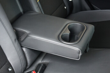 Fototapeta premium Leather trimmed anfolding armrest with cup holders in rear seats inside a vehicle. Electric car interior. Clean leather interior.