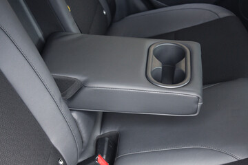 Leather trimmed anfolding armrest with cup holders in rear seats inside a vehicle. Electric car...
