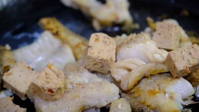Cooking Indoors pan grilled seasoned Cod fillets and Tofu with spices and sun-dried tomatoes. On Stovetop, iron cast skillet, close up boiled oil, process deep fried.