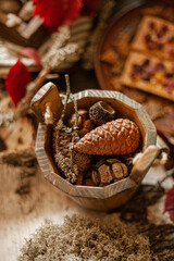 An idyllic fall Thanksgiving scene on a wooden table with leaves, twigs, pine cones and moss. Handcrafted decor and warm colors create a comfortable atmosphere.