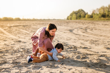 Young mother playing with her baby in the park, laughing and spinning him around on the sand