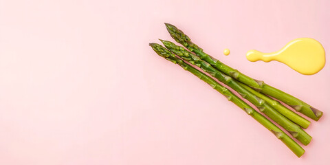 Fresh asparagus spears with a drizzle of yellow sauce on a soft pink background, showcasing a vibrant food aesthetic.