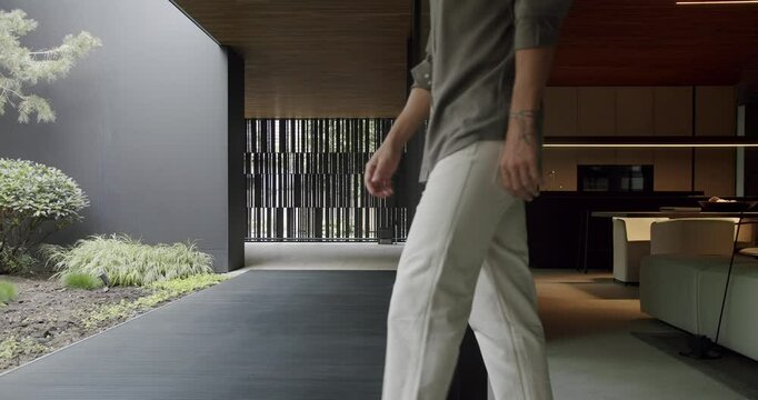 A stylish man steps into a sleek, contemporary home featuring minimalist design, a serene garden, and sophisticated interiors. Man Walking into a Modern Home with Minimalist Architecture