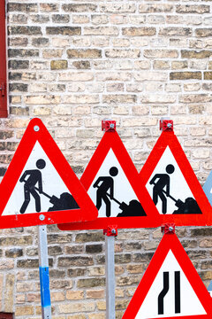Group of red triangular construction warning signs leaning against a brick wall, referencing roadwork, hazards, and temporary regulation in transit systems.