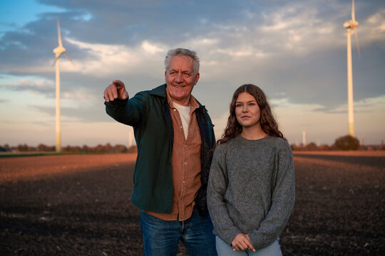 Grandfather and granddaughter in a field with wind turbines pointing and smiling