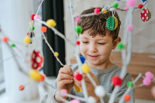 Child decorating an Easter tree with colorful ornaments at home