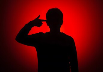 Silhouette of person gesturing suicide against a dramatic red backdrop