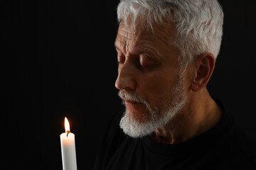 Sad senior man with burning candle crying on black background. Grieving loss