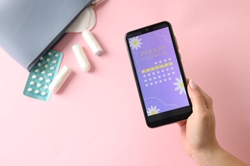 Menstruation. Woman holding smartphone with period calendar application on pink background, top view