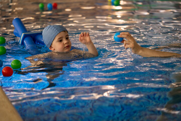 Child swimming with floatation device reaching for ball held by instructor