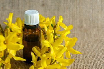A small amber glass bottle with a white cap, filled with essential oil, placed on a burlap surface,...