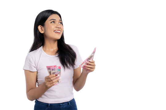 Optimistic young Asian woman holding Indonesian rupiah banknotes and looking up with hopeful expression, isolated on transparent background