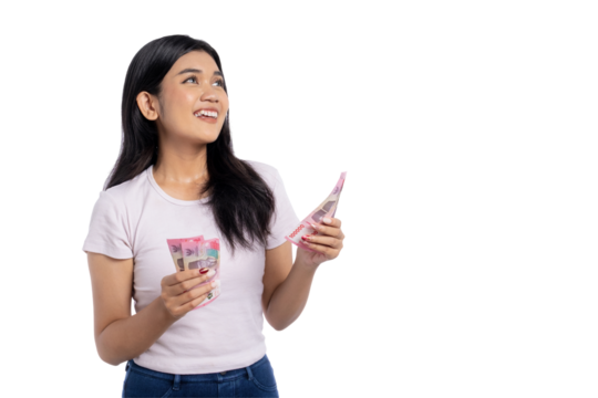 Optimistic young Asian woman holding Indonesian rupiah banknotes and looking up with hopeful expression, isolated on transparent background
