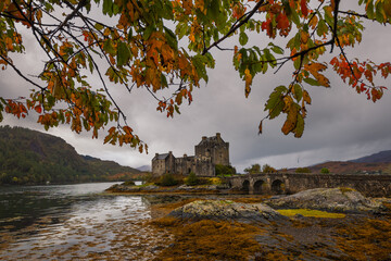 Eilean Donan Castle stands majestically amid autumn hues, its reflection shimmering in calm waters....
