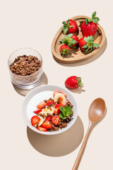 Greek yogurt with chocolate granola, strawberries and banana in a bowl on a yellow background