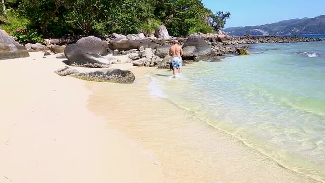 A man walks with his dog on the flat sand of Paradise Beach in Phuket