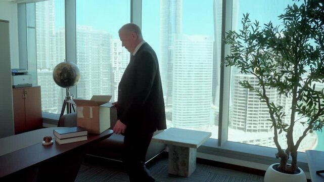 Senior man on the last day of work before retiring, packs up a box and leaves his dream office with sadness and nostalgia