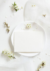 Blank card on plate near tulle and wild plums white flowers top view, romantic wedding mockup