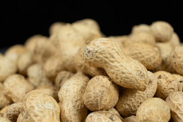 Pile of unpeeled peanuts in shell close-up on black background.