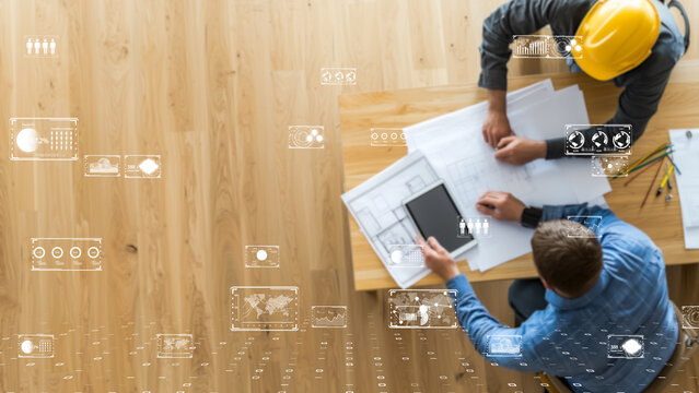 Engineers with safety helmets working with AI-driven construction data on blueprint desk