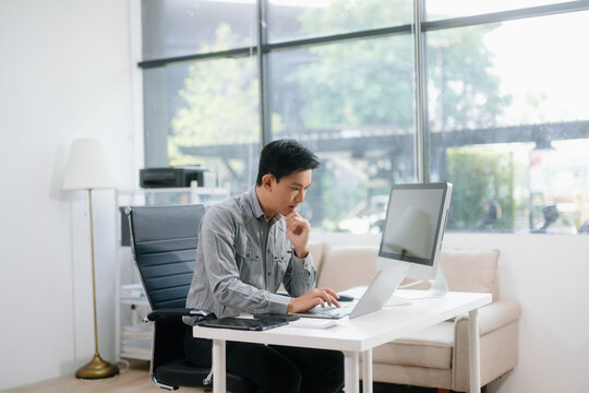 Confident businessman working on finance analysis with a tablet and laptop at office desk.
