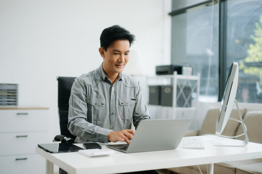Confident businessman working on finance analysis with a tablet and laptop at office desk. - Powered by Adobe