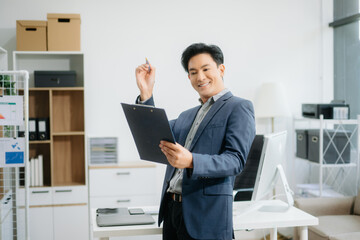 Naklejka premium Young attractive Asian man smiling thinking planning writing in notebook, tablet and laptop