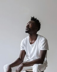 Obraz premium A contemplative man in a white outfit sits on a stool against a plain background, exuding calmness