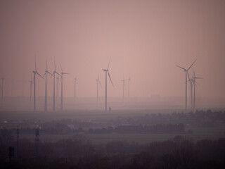 Obraz premium Wind turbines in a rural landscape during a hazy sunset, generating renewable energy in a calm and misty atmosphere, symbolizing sustainability and clean power.