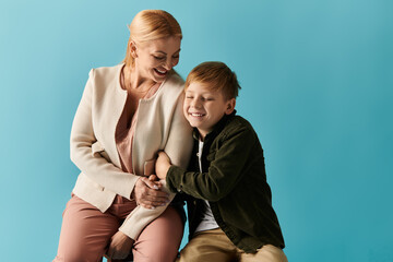 Mom and son share a joyful moment while sitting together against a vibrant blue backdrop