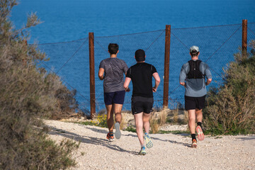 Three men running on coastal trail alongside scenic ocean view
