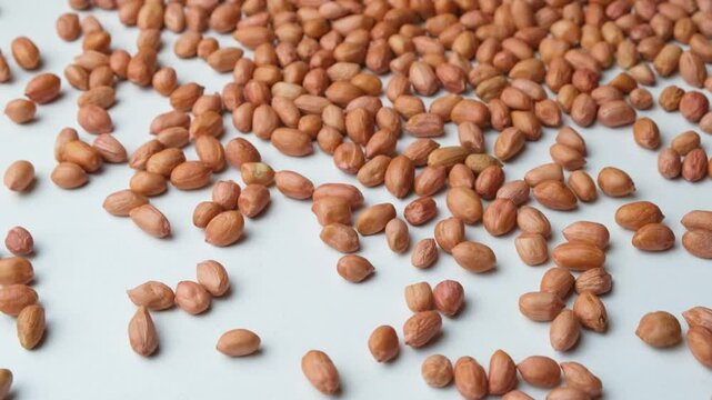Scattering of raw whole dried peanut kernels on a white background close-up slow motion
