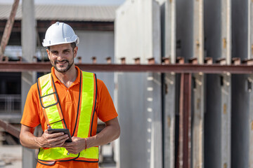 Male civil engineer is using tablet or smart phone conducting a quality check in a precast factory. Engineer in safety suit working in a construction factory.