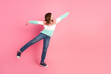 Playful adorable girl in a colorful sweater and jeans posing against a pink background, expressing...