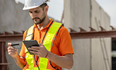 Male civil engineer is using credit card to pay online bill through tablet or smart phone in a construction factory. Online payment