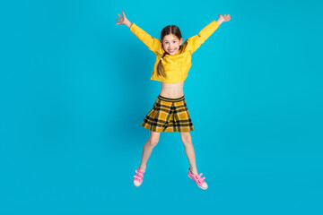 Smiling adorable young girl in casual fashion jumping with joy on a blue background