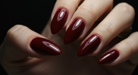 Close up of hand showing dark red stiletto nails against a dark background in studio lighting