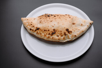 Deliciously baked calzone on a white plate against a dark background