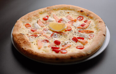 Delicious salmon pizza with cherry tomatoes and a slice of lemon on a plate