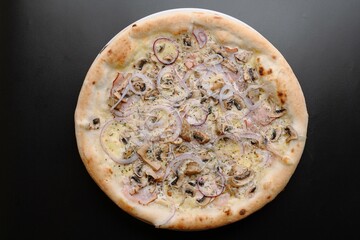 Delicious pizza topped with mushrooms, ham, and onions on a dark background