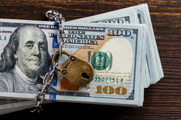 Metallic chain and padlock around american one hundred dollar banknotes, closeup, top view....