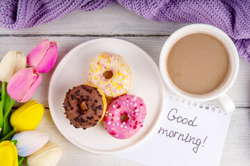 Small sugar glazed donuts with coffee latte cup, tulip flowers, sweater, tulip flower bouquet and note Good Morning. Spring holiday, Mother Day, Woman day, Birthday greeting card background 